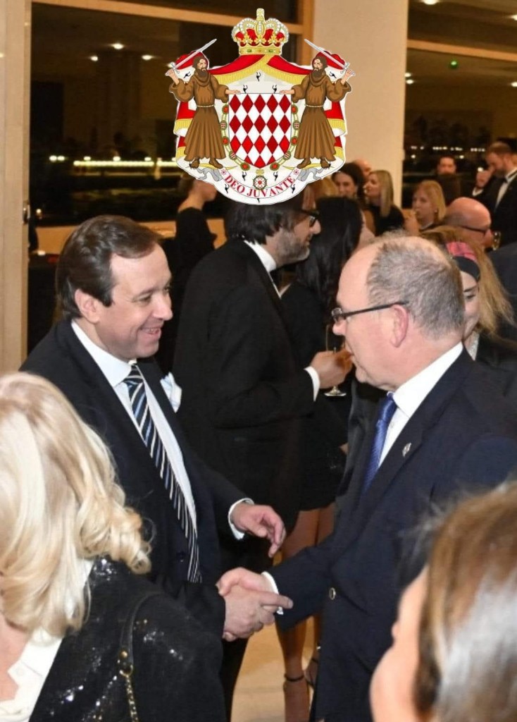 Two men shake hands at a formal event, with a crowd in the background and a crest above them.