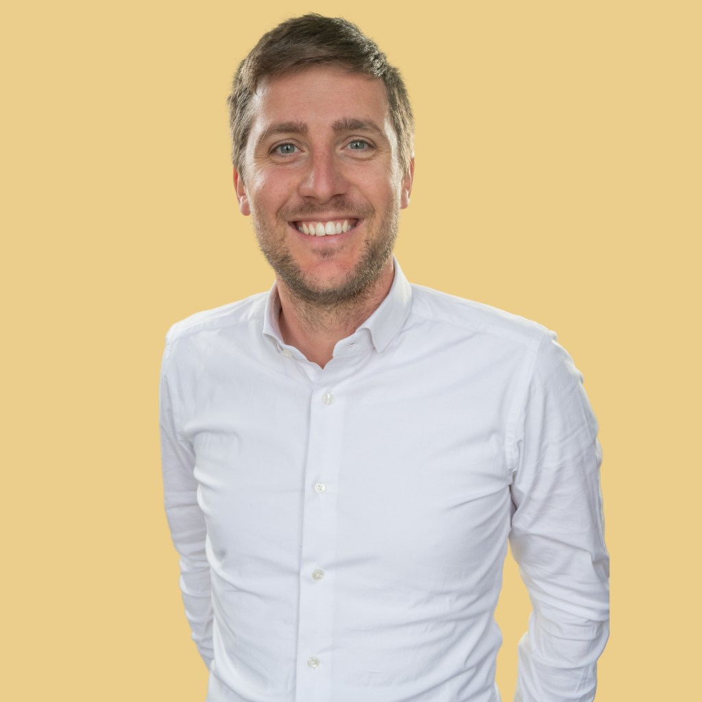Portrait of a smiling man in a white shirt against a yellow background.