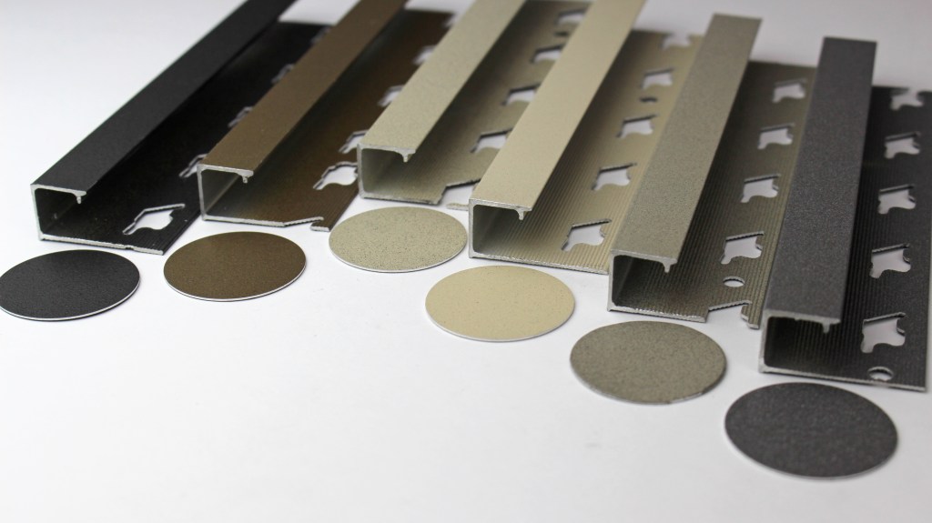 An assortment of aluminum profiles in different finishes including black, gold, and gray, alongside circular samples that showcase color and texture variations.