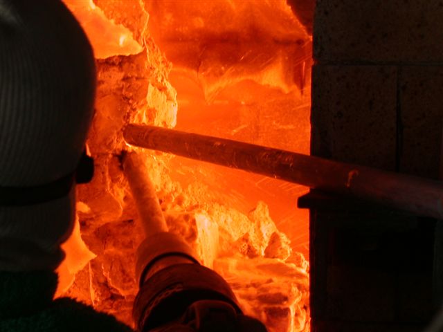 A specialized technician, equipped with full thermal protective gear, precisely maneuvers a ceramic welding lance.