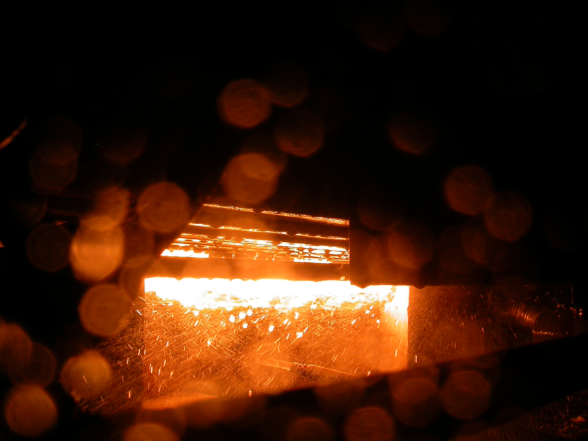 An artistic close-up of sparks and intense heat radiating from the dark opening of an industrial furnace.