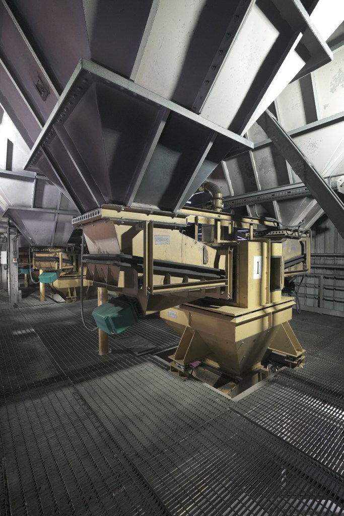 Industrial interior view of a material handling system used in steel manufacturing, featuring multiple hoppers and conveying equipment.