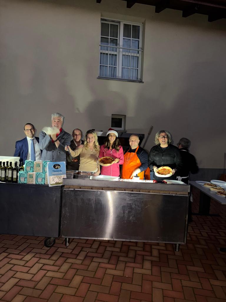 A group of individuals standing behind a serving table, smiling and holding pizzas, celebrating at a reception center.