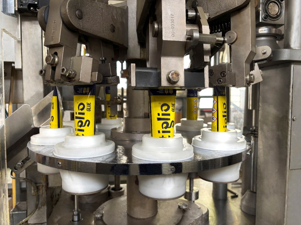 Close-up of a machine filling tubes with glue, showcasing multiple glue tubes being processed in a production line.